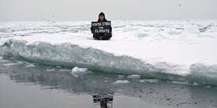 Auf einer Eisscholle sitzt ein Mensch mit einem Demoschild