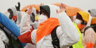 Aktivistin mit weißem Maleranzug und orangenem Halstuch und Atmenschutzmaske