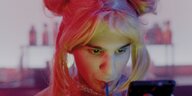 Hauptfigur Parvis mit Sailormoon-Perücke trinkt gerade aus einem Strohhalm und schaut aufs Handy