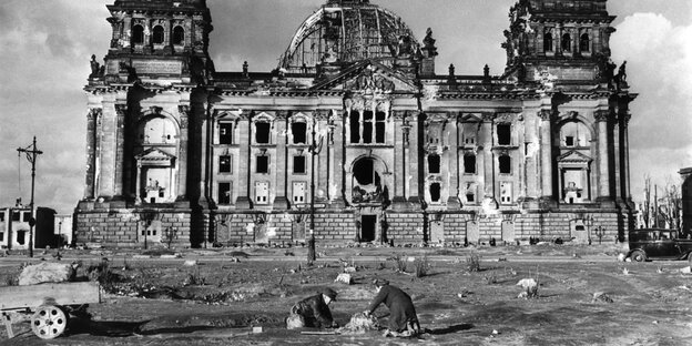 Der Reichstag nach dem 2. Weltkrieg. Davor zwei Menschen, die nach Brennholz graben