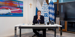 CSU Chef Markus Söder sitzt an seinem Schreibtisch, an der Wand hängt ein Holzkreuz, rechts von ihm ist eine Büste von Franz Josef Strauss.