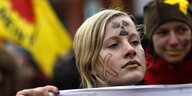Eine Frau hat sich das Radioaktivität-Zeichen auf die Stirn gemalt
