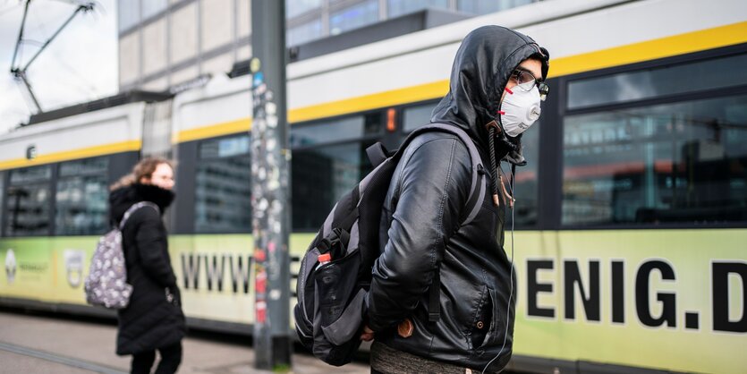 Ein Mann mit Kapuze und Atemmaske steht vor einer Straßenbahn auf dem Alexanderplatz in Berlin