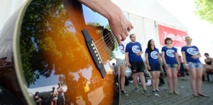 Im Vordergrund eine Gitarre, im Hintergrund singende Jugendliche
