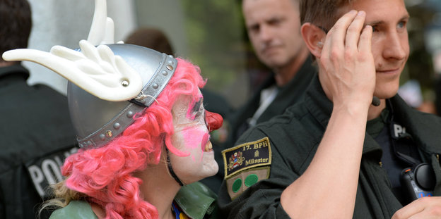 Eine Frau in Clownsmaske neben einem Polizisten