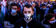 Ein Demonstrant mit Anonymous Maske steht im Vordergrund und hinter ihm befinden sich zahlreiche weitere Demonstranten