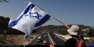 Eine Person steht auf einer Brücke und hält eine israelische Flagge in der Hand.