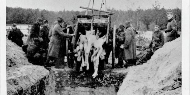 Sowjetische Kriegsgefangene kippen im Winter 1941/42 Leichen in ein Massengrab in Bergen-Belsen und werden dabei von Soldaten der Wehrmacht bewacht.