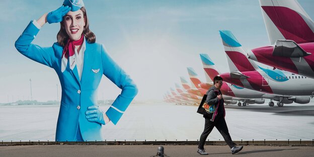 Eine Frau läft vor einer Werbetafel von Eurowings auf der eine Stewardess und Hecks von Flugzeugen zu sehen sind.