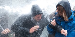 Personen werden vom Wasserstrahl eines Polizeifahrzeugs getroffen