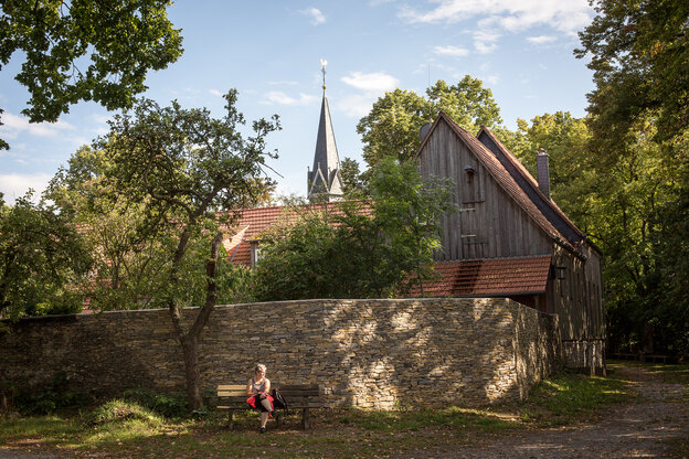Ein Frau sitzt auf einer Bank vor dem Kloster Hülfensberg Ein Frau sitzt auf einer Bank vor dem Kloster Hülfensberg