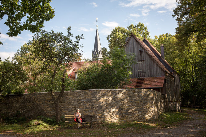 Ein Frau sitzt auf einer Bank vor dem Kloster Hülfensberg