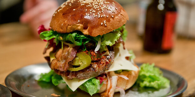 Ein Burger mit Blattsalat und Hackfleisch liegt auf einem Metallteller.