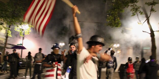 Ein schwarzer Demonstrant schwenkt eine USA-Flagge und muss wegen Tränengaseinsatz husten