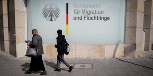 Zwei Menschen gehen am Bundesamt für Migration und Fluechtlinge in Berlin vorbei