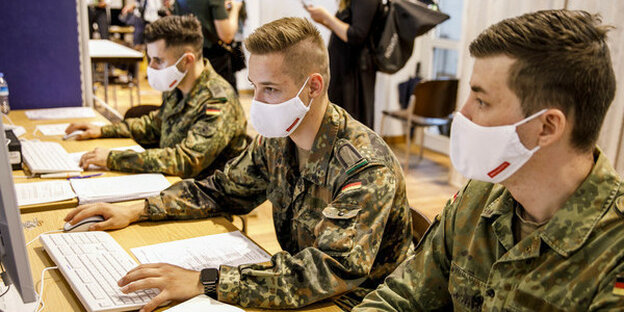 Drei uniformierte Soldaten arebiten mit Masken an Computern