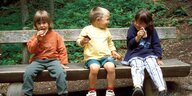 Drei Kinder sitzen auf einer Bank, essen Milchschnitte und kaspern rum.