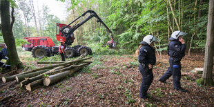 Ein roter Harvester und zwei behelmte Polizisten zwischen Bäumen