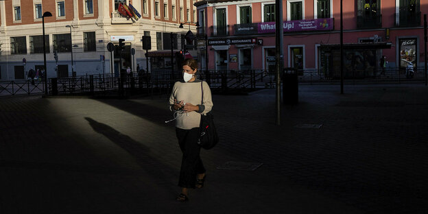 Eine Frau mit Mundschutzmaske ist allein auf einem städtischen Platz