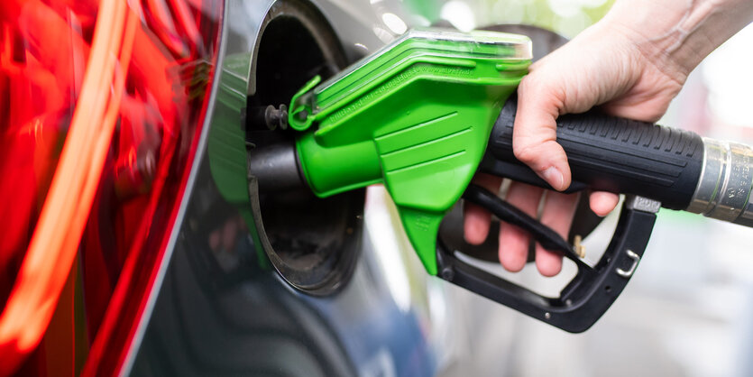 Eine Hand hält die Zapfpistole einer Tankstelle in den Tank eines Autos