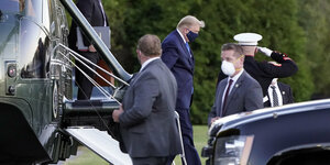 Donald Trump steigt aus einem Hubschrauber aus. Er trägt Anzug und eine Gesichtsmaske