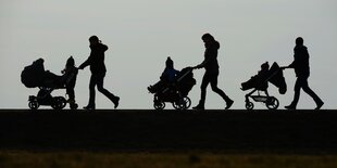 Schatten von drei Personen, die mit Kinderwägen hintereinander laufen