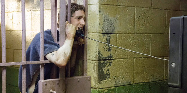 Mann hinter Gittern mit einem Telefon in der Hand