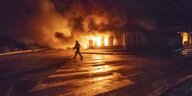 Eine Person geht in der Nacht an einem brennenden Gebäude vorbei.