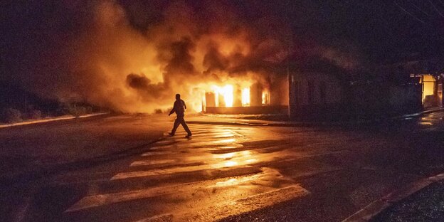 Eine Person geht in der Nacht an einem brennenden Gebäude vorbei.
