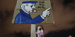 Frau mit Maske hält Plakat "Go to jail"