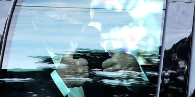 Donald Trum mit Atemschiutzmaske hinter der Fensterscheibe eines Autos