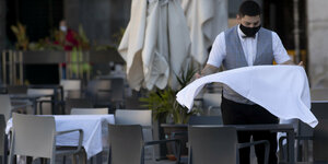 Kellner schüttelt Tischdecke auf in leerem Restaurant