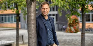 Stefan Kleinschmidt lehnt mit der rechten Schulter an einem Baum und lächelt in die Kamera