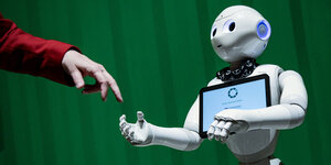 Ein Roboter interagiert mit einer Frau, in dem er die Hand nach ihr ausstreckt