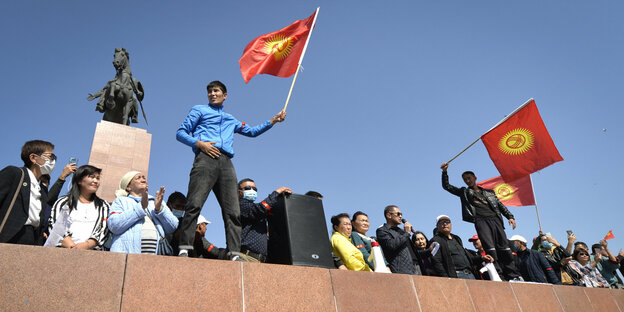 Menschen schwenken die kirgisische Flagge auf einem Sockel.