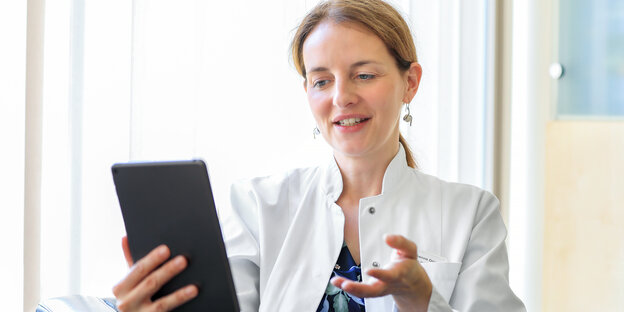 Eine junge Frau im weißen kittel der Ärztin spricht in ihr iPad