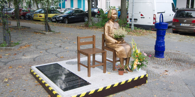 Bronzestatue einer jungen Frau, die auf einem Stuhl sitzt.