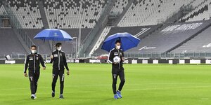 Schiedsrichter laufen vor dem dann abgesagten Spiel mit Regenschirmen über den Rasen