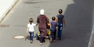 eine Frau geht mit Kinderwagen und drei Töchtern an der Hand