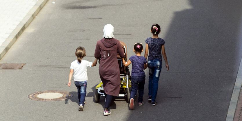 eine Frau geht mit Kinderwagen und drei Töchtern an der Hand