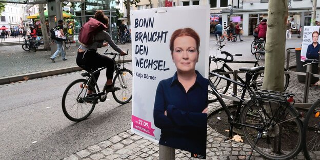 Wahlplakat von Katja Dörner hängt an einem Mast, im Hintergrund Fahrradfahrer