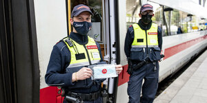 Zwei Beamte der Deutschen Bahn verteilen Masken an Fahrgäste