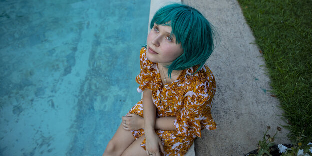 Mädchen mit türkiser Perücke an einem Pool sitzend