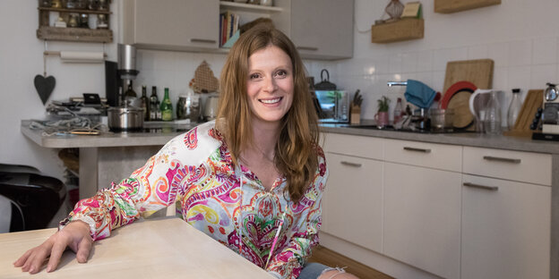 Eine junge Frau mit langen braunen Haaren sitzt am Küchentisch