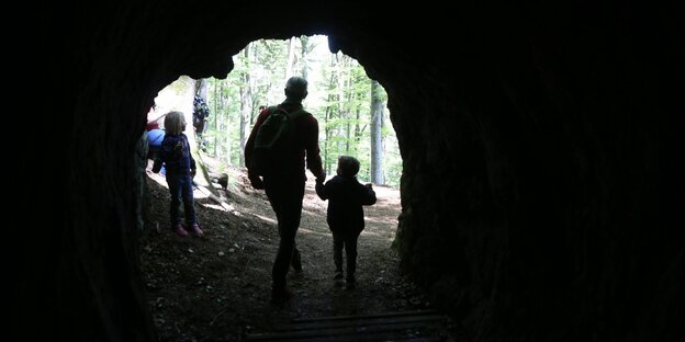 Vater mit Kindern an der Hand geht durch eine Hohle im Wald