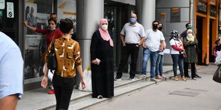 Menschen stehen mit Masken vor einem Supermarkt und warten