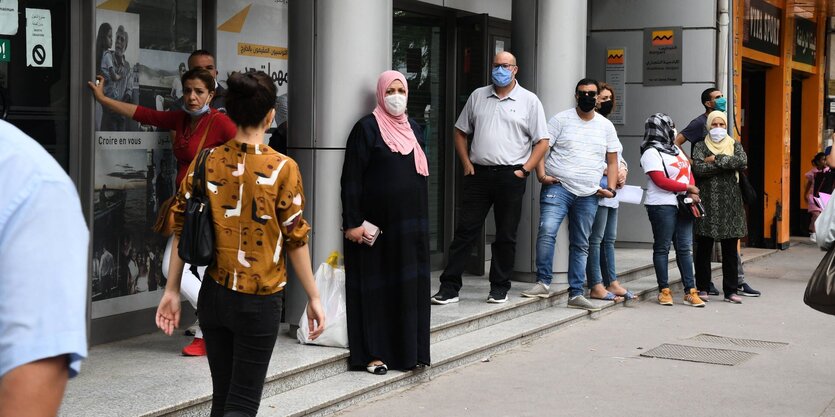 Menschen stehen mit Masken vor einem Supermarkt und warten