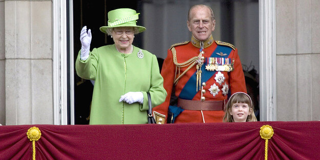 Die englische Queen steht mit ihrem Mann auf einem Balkon.
