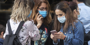 Drei Frauen, zwei beschäftigen sich mit ihren Smartphones.