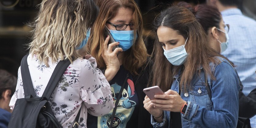 Drei Frauen, zwei beschäftigen sich mit ihren Smartphones.